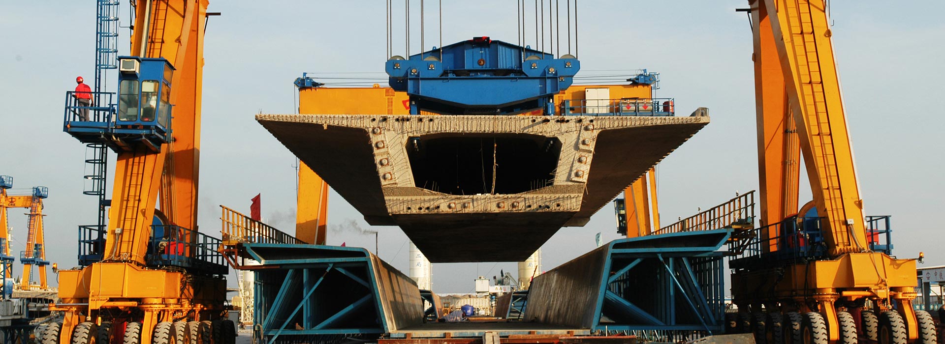 Gantry crane lifting precast girders using specialized spreaders for safe load distribution in precast yard