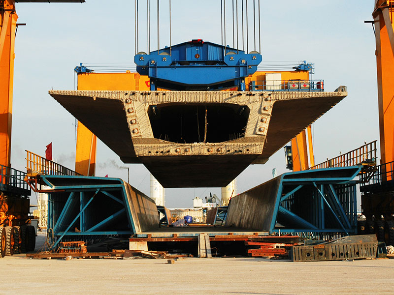 Gantry crane lifting precast girders using specialized spreaders in a precast yard