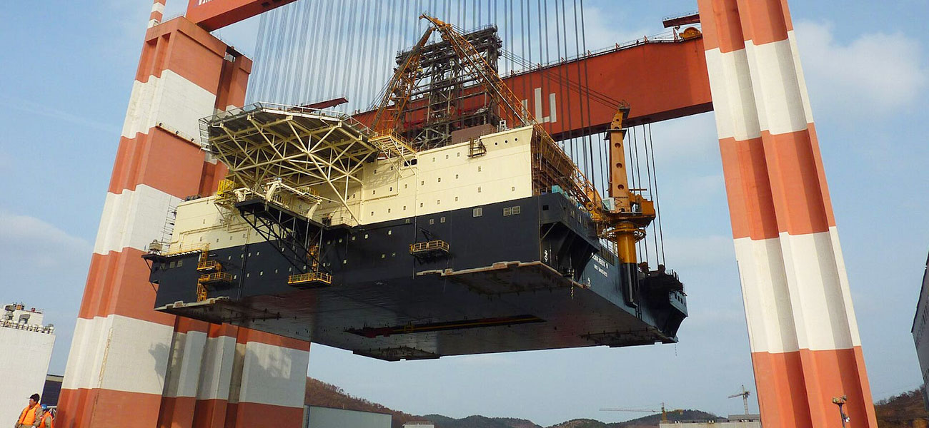 Goliath crane lifting a large ship block in shipyard during block assembly and erection stage.