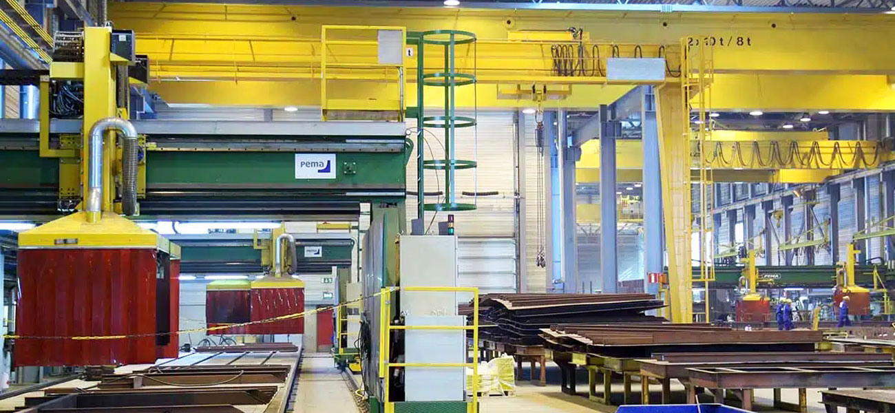 Overhead cranes handling steel plates in shipbuilding fabrication workshops