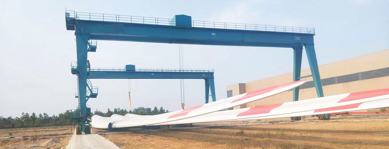 Two rubber tyred gantry cranes collaboratively lifting a wind turbine blade